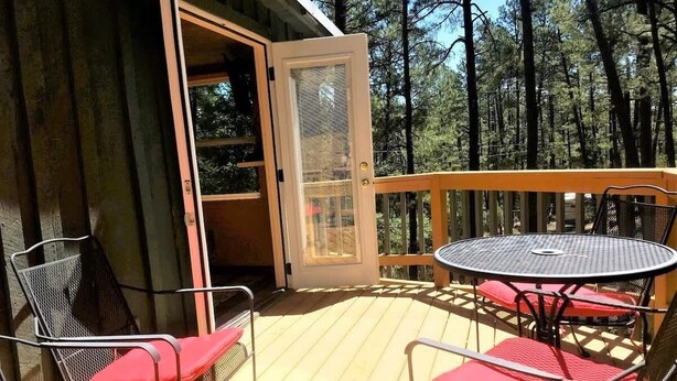 Eine HolzdTerrasse mit Tisch und Stühlen, eine Tür zu einem Innenraum und ein bewaldeter Hintergrund.