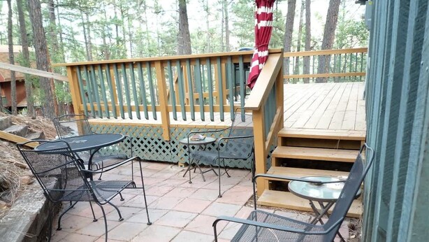 A patio with metal chairs and a table, surrounded by a wooden deck and a railing.