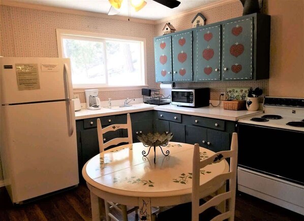 Een kleine keuken met een koelkast, magnetron, fornuis en een eettafel met stoelen.