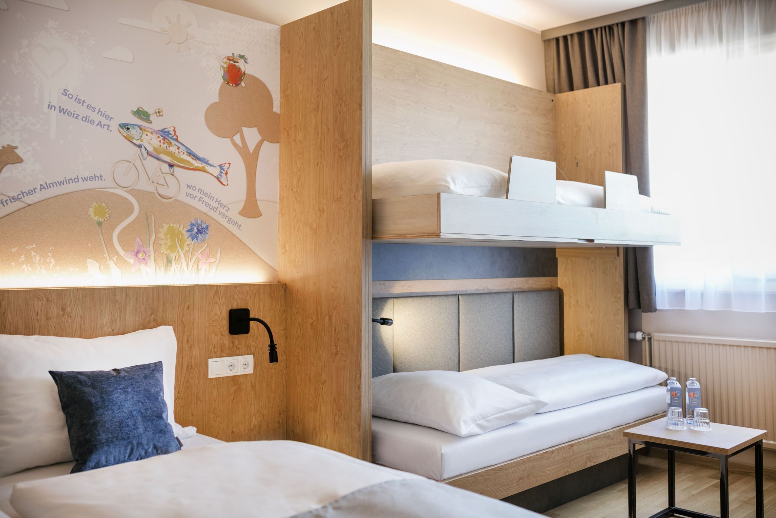 A hotel room with a bunk bed, a small table with water bottles, and a wall with a nature-themed mural.
