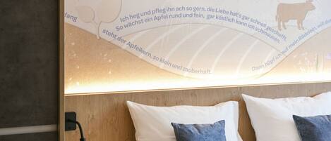A hotel room with a large wall mural, a neatly made bed with white and blue pillows, and a small wooden nightstand.