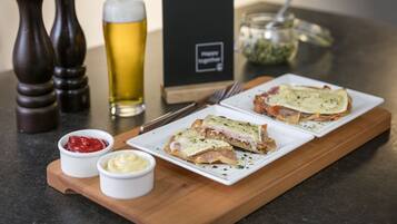 Une planche de service en bois avec deux sandwichs, deux petits bols de condiments, un verre de bière et un présentoir à menus.