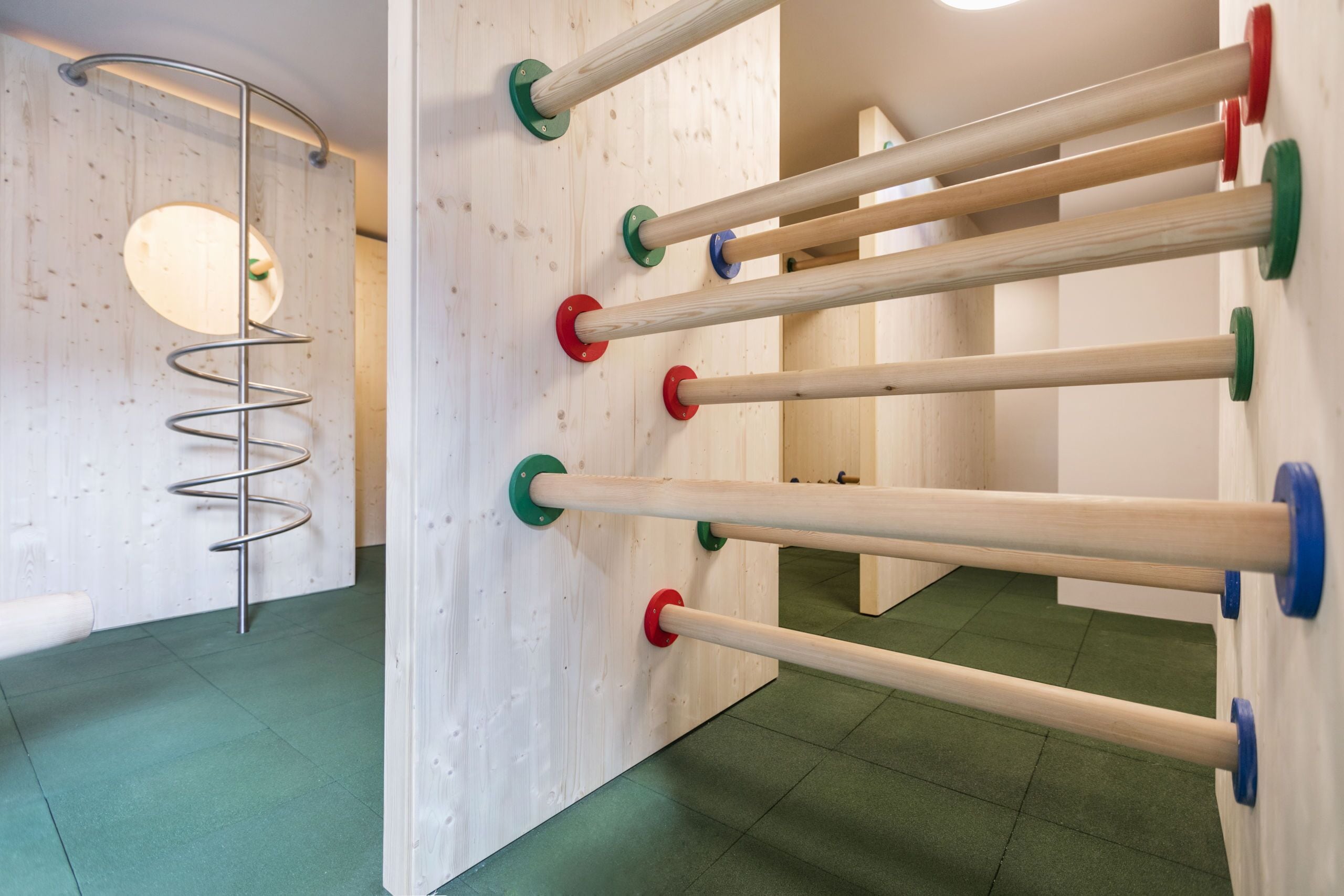 Een kamer met houten wanden, een spiraalvormige metalen constructie en meerdere houten palen met gekleurde voetstukken.