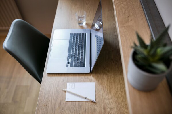 A laptop on a wooden desk with a glass of water, a notepad, and a pen. - JUFA Hotel Weiz (Weiz)