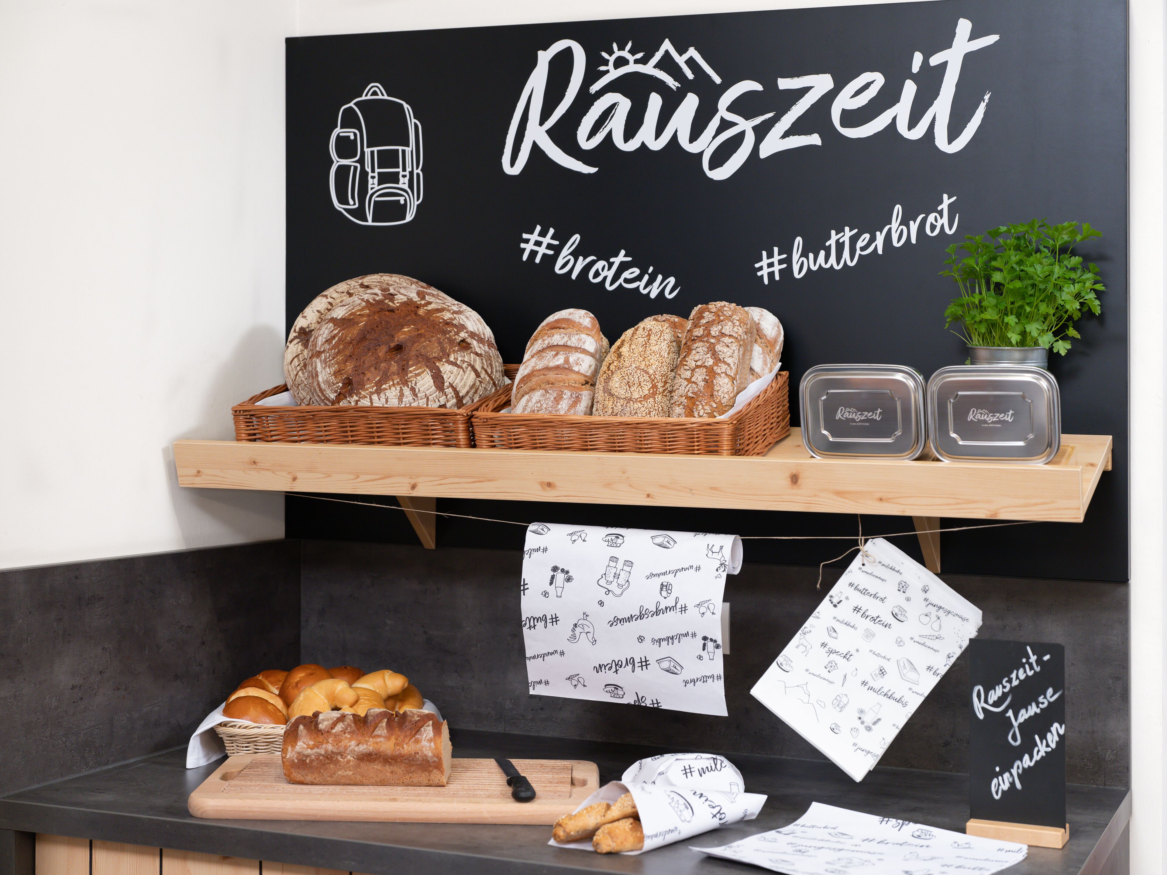 A bakery display with various breads and pastries, a chalkboard sign with the word "Räuszeit" and hashtags, and a wooden cutting board with a knife.