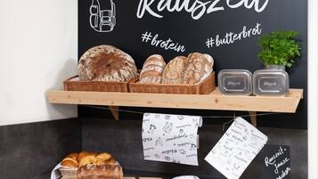 A bakery display with various breads and pastries, a chalkboard sign with the word "Räuszeit" and hashtags, and a wooden cutting board with a knife.