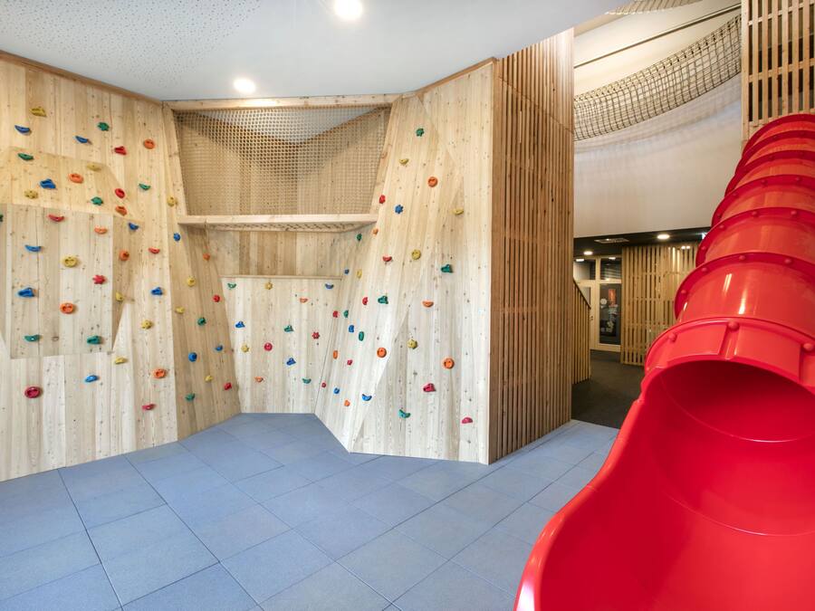 Un mur d’escalade équipé de différentes prises et d’un toboggan rouge.