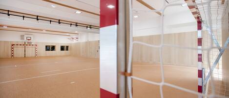 An indoor sports hall with a basketball court, a netted goal area, and wooden flooring.