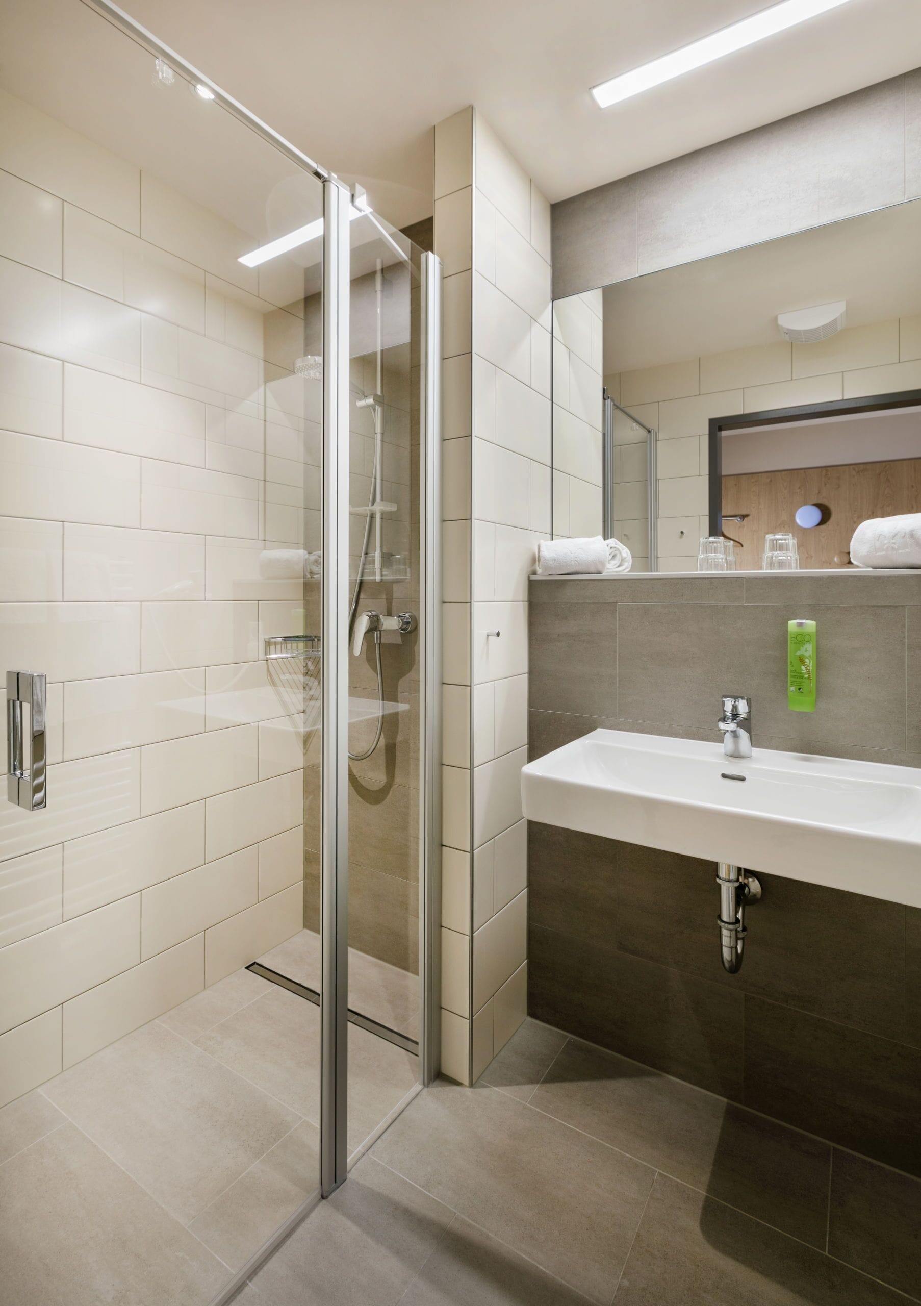 A modern bathroom with a glass-enclosed shower, a white sink, and a mirror above it.