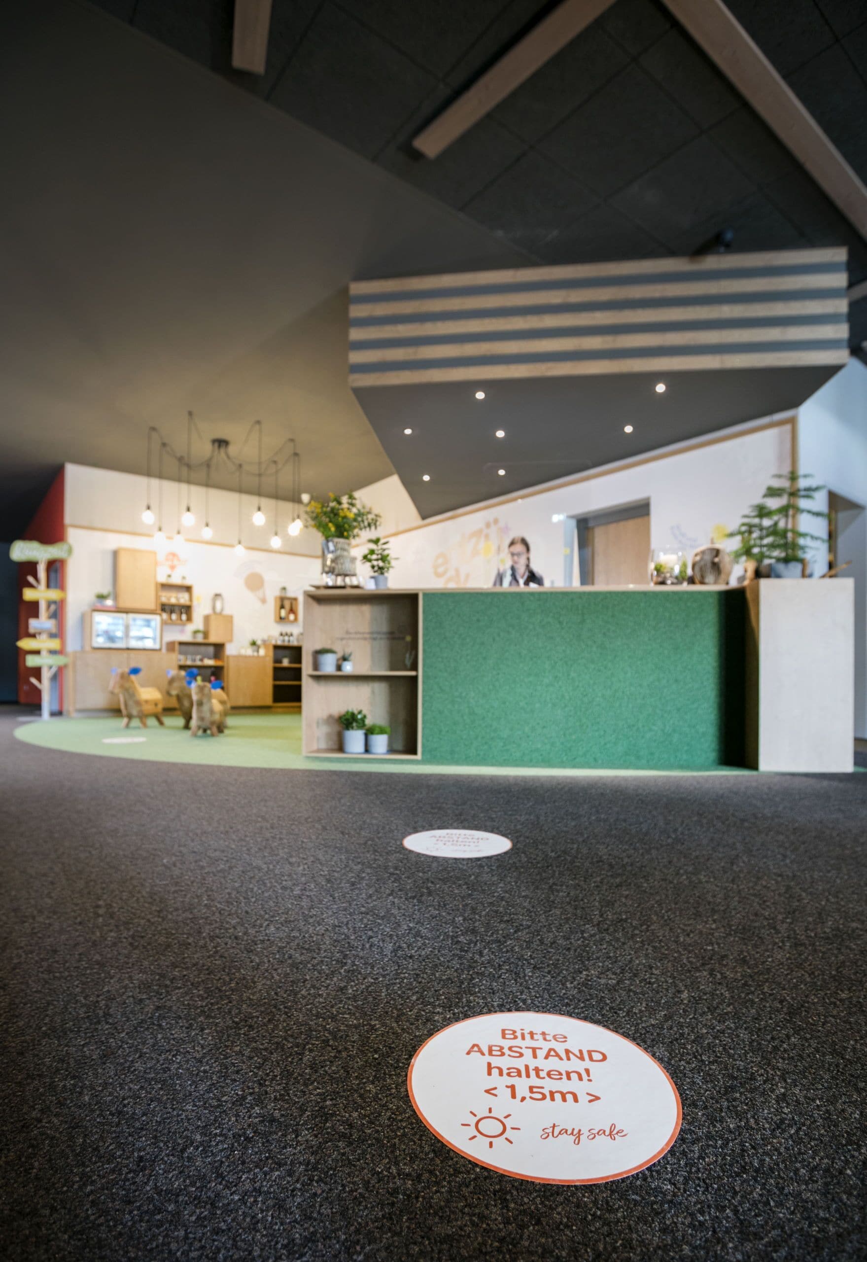A reception area with a green counter, a sign indicating a 1.5m social distancing measure, and a floor mat with a similar message.