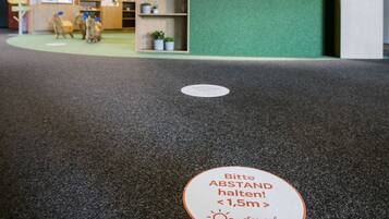A reception area with a green counter, a sign indicating a 1.5m social distancing measure, and a floor mat with a similar message.