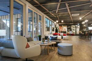 Um interior moderno com teto alto, janelas amplas e diversos espaços de estar, incluindo sofás e uma mesa redonda.