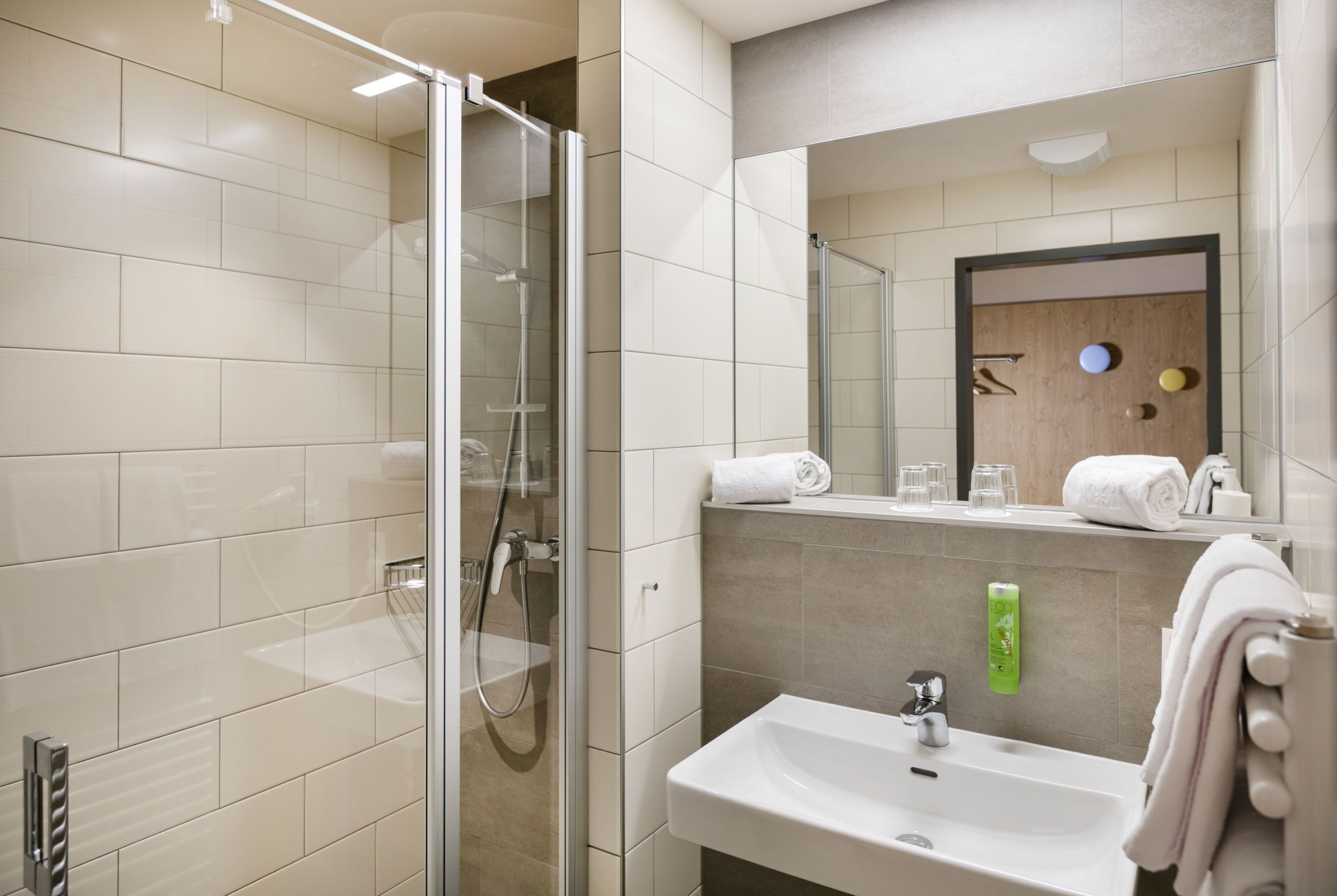 Un baño moderno con cabina de ducha de vidrio, un lavabo con espejo y un perchero para toallas.