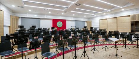 A spacious hall with rows of chairs and music stands, a red banner with a logo, and a wooden panel wall.