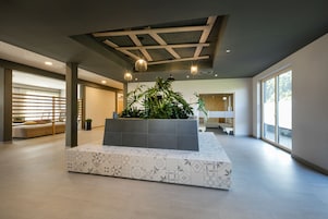 Um hall amplo com um vaso de plantas central, escada e grandes janelas.