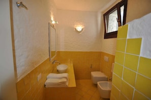 A bathroom with a sink, toilet, and bidet, featuring yellow and white tiles and a mirror. - Villa Lara 2 (Arzachena)