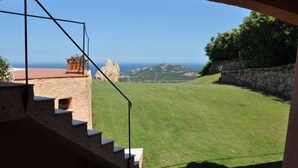 A view from a balcony with a stone staircase leading to a terrace overlooking a grassy area and the sea. - Villa Lara 3 (Arzachena)