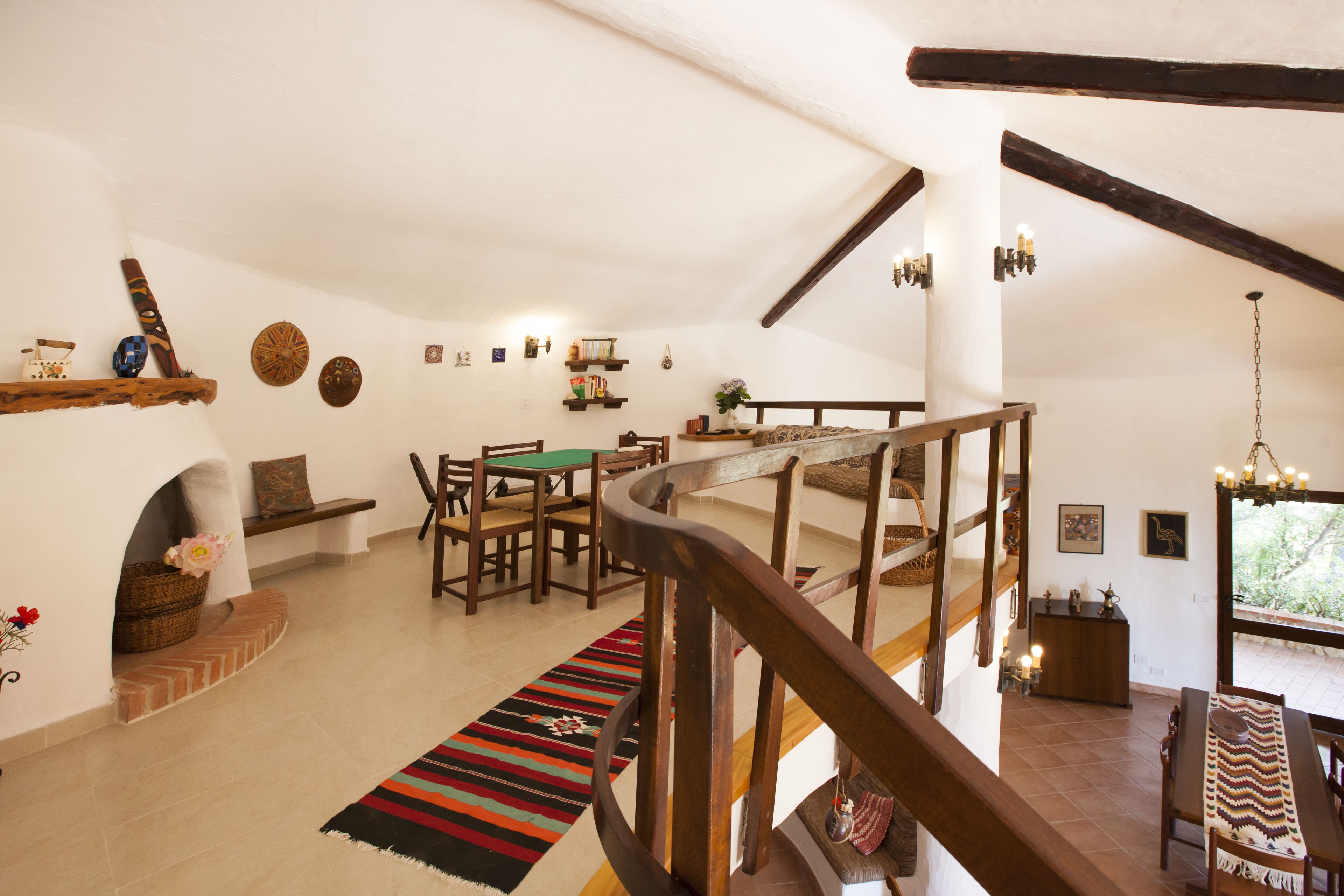 A spacious loft with a high ceiling, wooden beams, a dining area with a green table, and a staircase leading to an upper level.