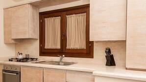 Eine moderne Küche mit hellen Holzschränken, einem Gasherd, einer Spüle und einem Fenster mit Vorhängen.
