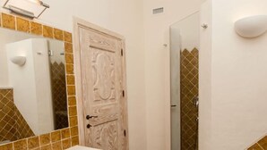 Ein Badezimmer mit weißem Waschbecken, einem Spiegel, einer Holztür und einer Duschkabine.