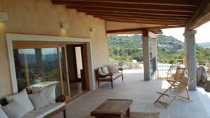 A covered outdoor seating area with a sofa, chairs, and a table, overlooking a mountainous landscape. - Villa La Silvaredda (Arzachena)