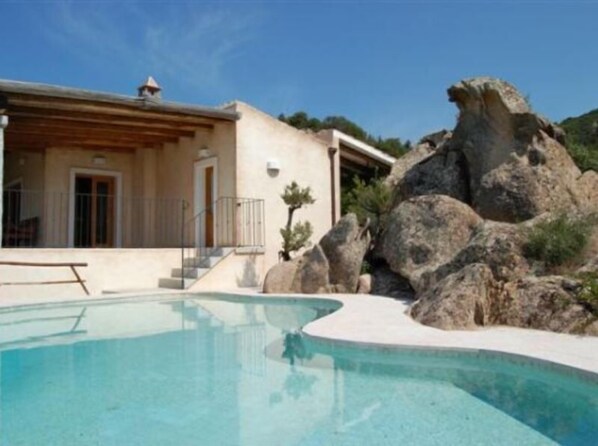 Ein modernes Haus mit Swimmingpool, umgeben von großen Felsen und Grünflächen.