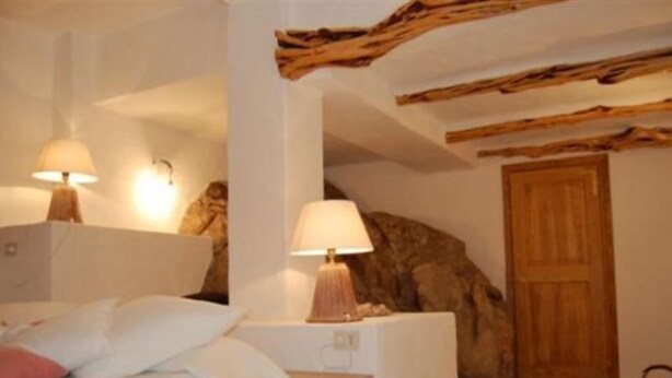 A bedroom with a bed, two bedside lamps, a wooden door, and a stone wall. - Villa La Silvaredda (Arzachena)