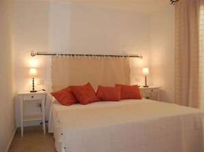 Ein Schlafzimmer mit einem Bett, zwei Nachttischen mit Lampen und einem Fenster mit Vorhängen.