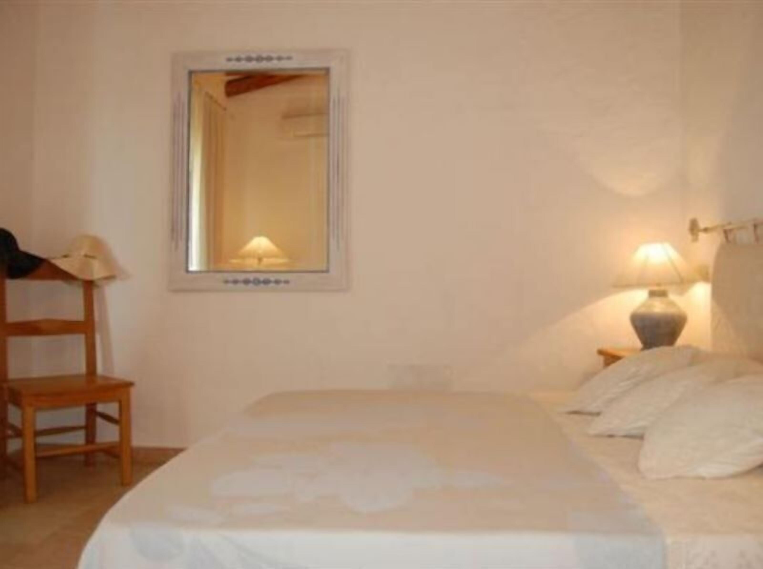 Ein Schlafzimmer mit Bett, Stuhl, Nachttisch, Lampe und Spiegel an der Wand.