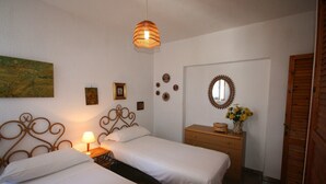 Une chambre avec deux lits simples, une table de chevet avec une lampe, une commode avec un miroir et une porte.