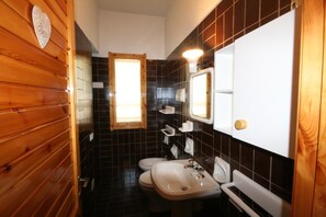 A compact bathroom with a wooden door, a white sink, a mirror, and a toilet. - Villa Luisa (Quartu Sant'Elena)