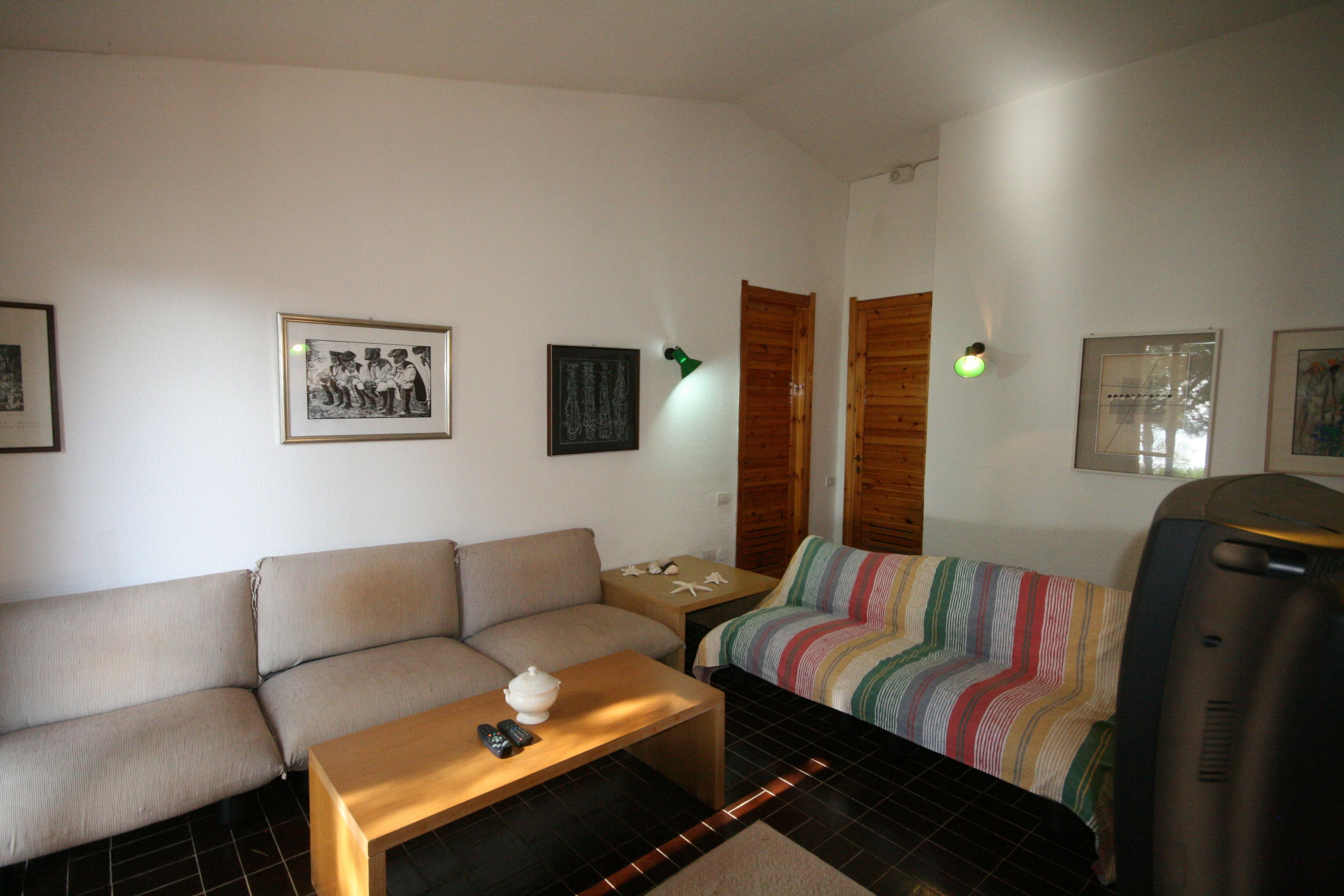 Una sala de estar con un sofá, una mesita con un control remoto, una manta a rayas colorida y cuadros en la pared.