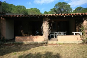A building with a tiled roof, a covered patio with outdoor furniture, and a small tree in the foreground. - Villa Luisa (Quartu Sant'Elena)