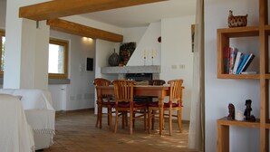 Un coin repas avec une table et des chaises en bois, une cheminée en pierre et une bibliothèque contenant des livres et des objets décoratifs.