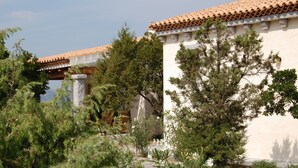 Un bâtiment doté d’un toit en tuiles et de murs blancs, entouré de verdure et d’arbres.