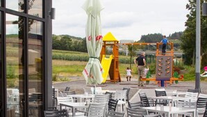 Um café ao ar livre com mesas e cadeiras, uma estrutura de recreação amarela e vista para o campo.