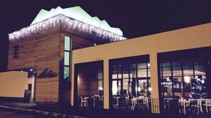 Um edifício com fachada de madeira e janelas amplas, provavelmente um restaurante ou café, com mesas ao ar livre.