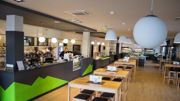 Um café moderno com área de bar, mesas de madeira e detalhes em verde.