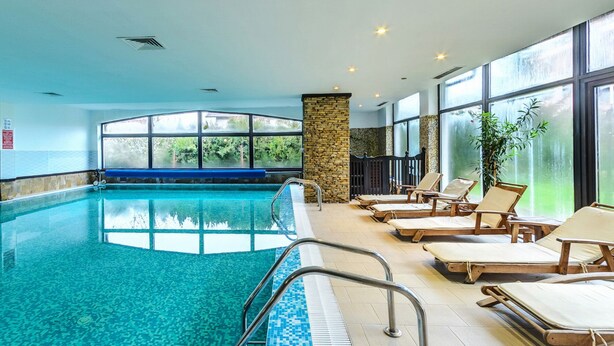 An indoor swimming pool with clear water, surrounded by lounge chairs and large windows offering views of greenery.