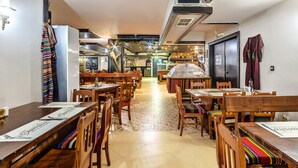 A restaurant with wooden tables and chairs, a tiled floor, and a central counter.