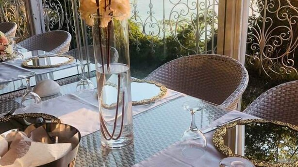 Un espace extérieur aménagé pour les repas, avec des chaises en osier, une table en verre et une vue sur la mer.