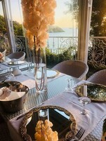 An outdoor dining area with wicker chairs, a glass table, and a view of the sea.