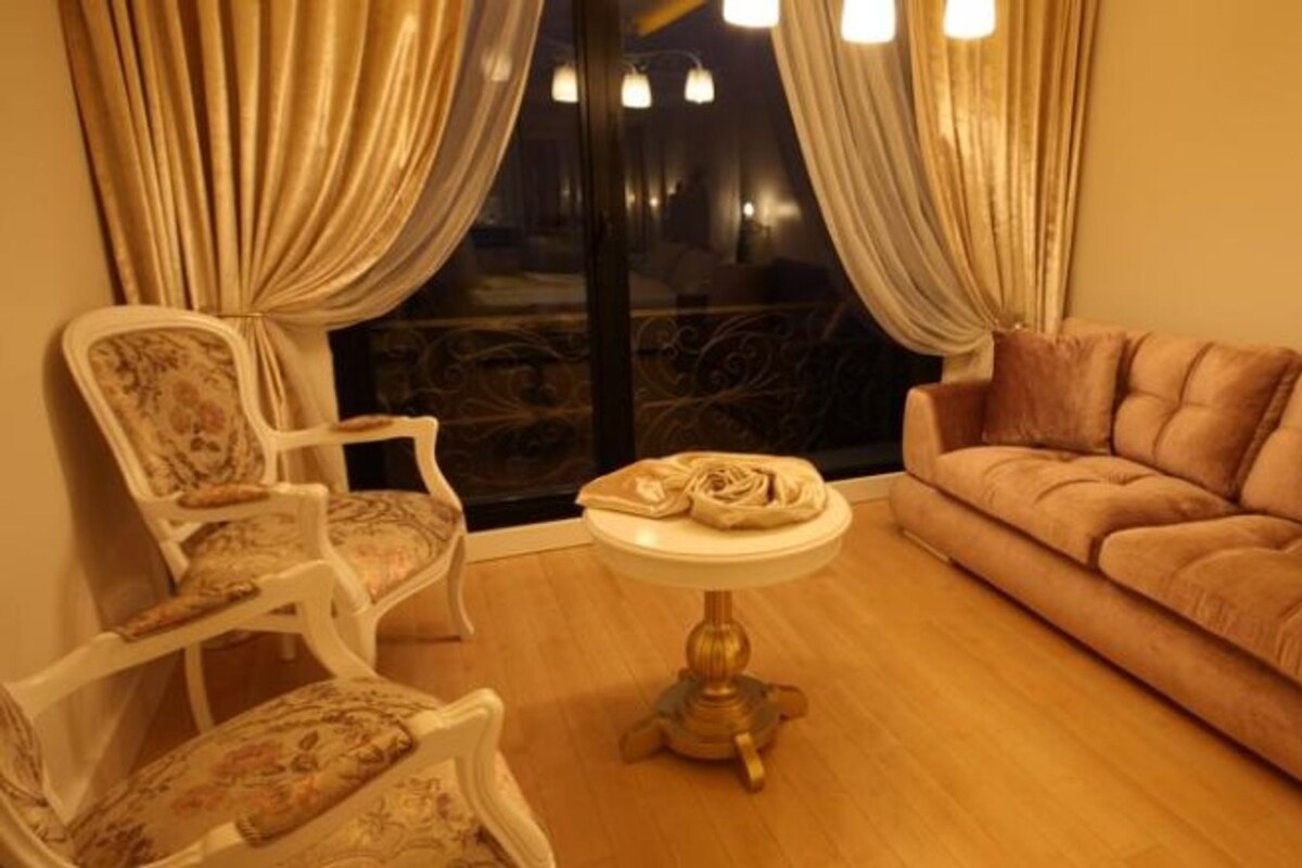 A room with a sofa, two chairs, a small round table, and a window with curtains.