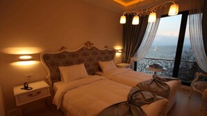 Une chambre dotée d’un grand lit, de tables de chevet, d’une commode, d’une chaise et offrant une vue sur la mer depuis un balcon.