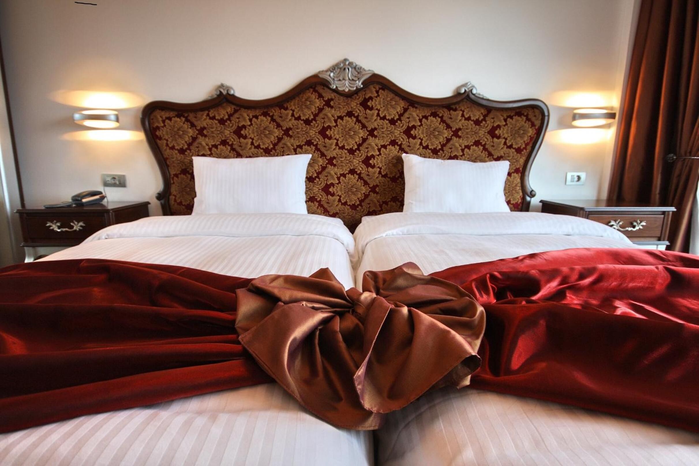 Un lit double avec une couverture rouge, deux oreillers blancs et une tête de lit en bois ornée d’un motif floral.