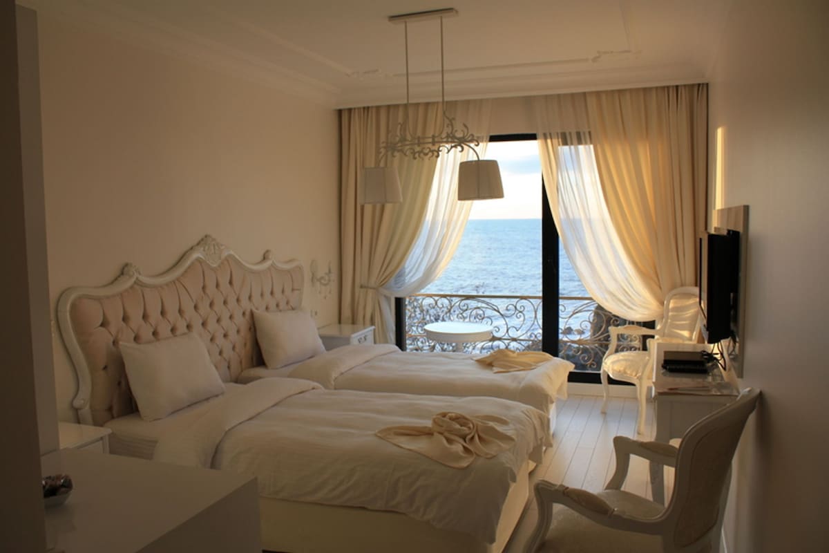 A hotel room with two beds, a balcony with a view of the sea, a desk with a chair, and a television.