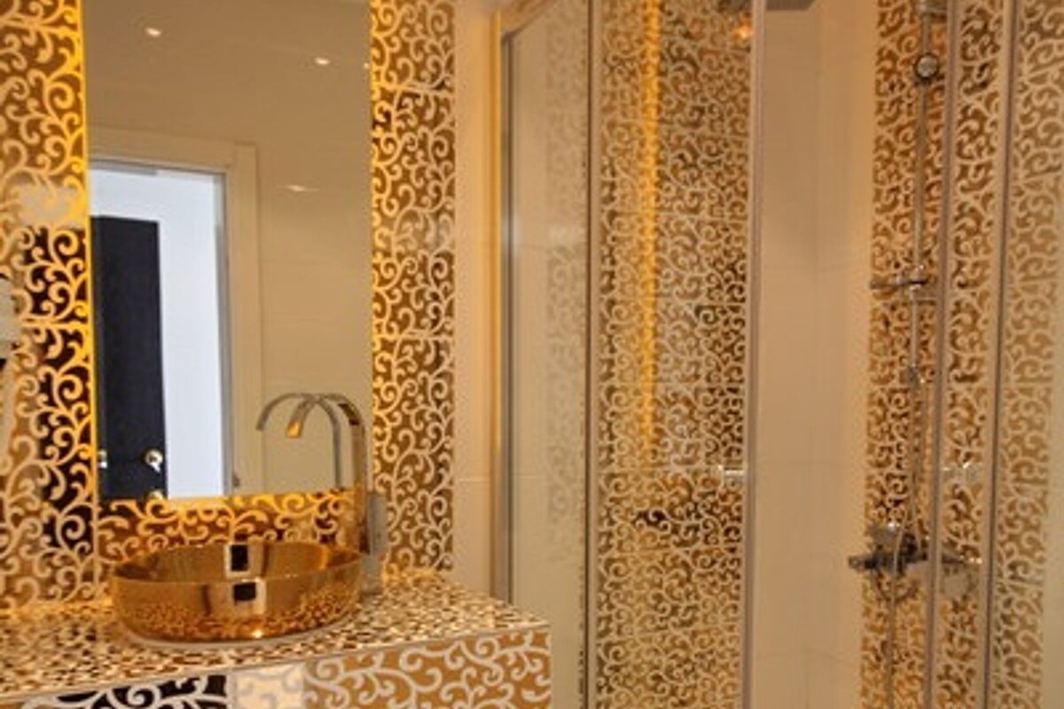 A bathroom with a patterned shower enclosure, a sink with a gold-colored basin, and a mirror.
