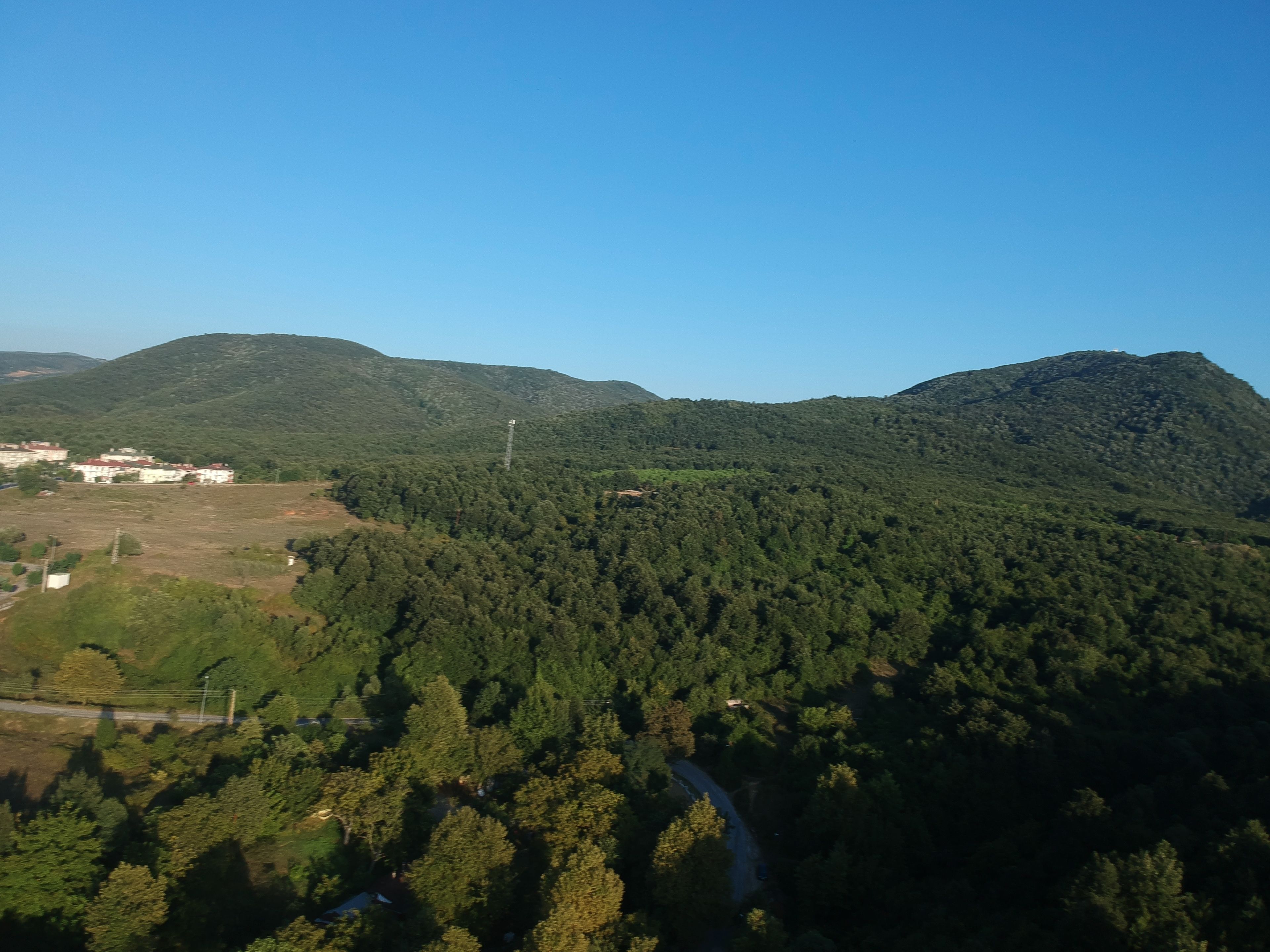 Eine gebirgige Landschaft mit dichtem Wald, einer kurvenreichen Straße und ein paar Gebäuden in der Ferne.