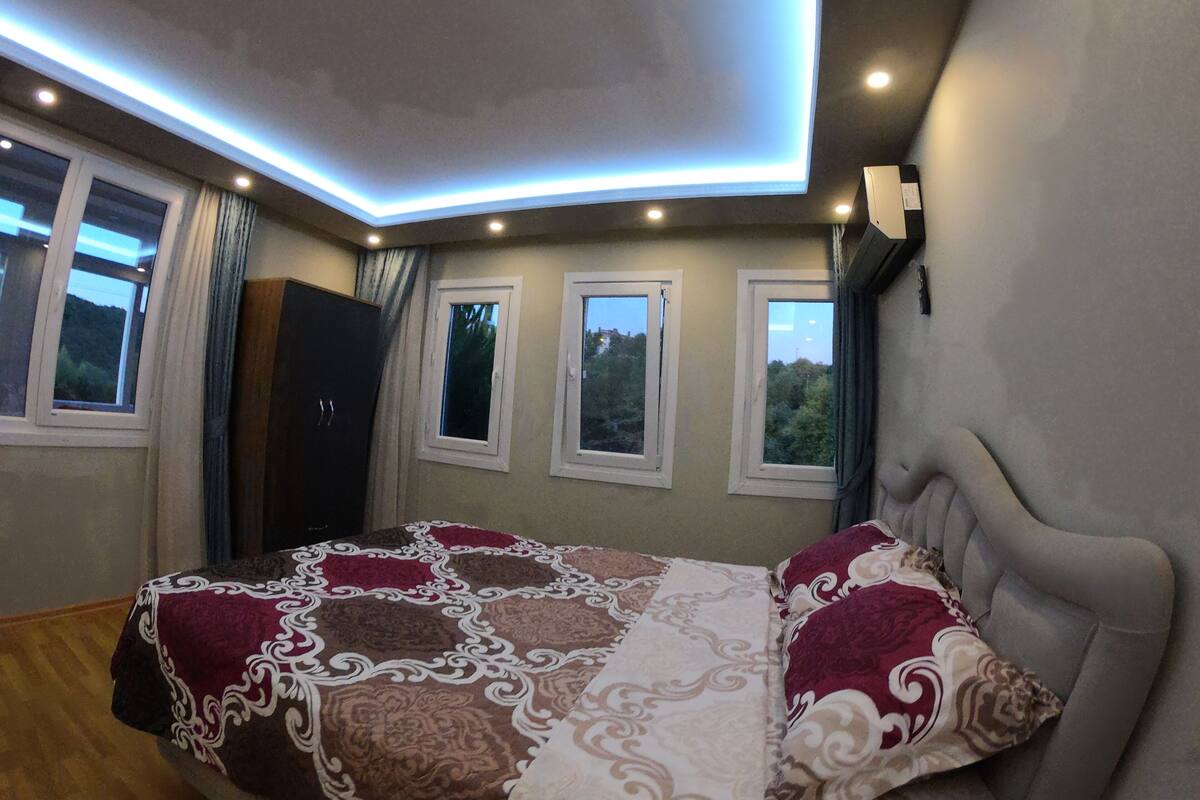 Ein Schlafzimmer mit einem Bett, einer Deckenleuchte und drei Fenstern.