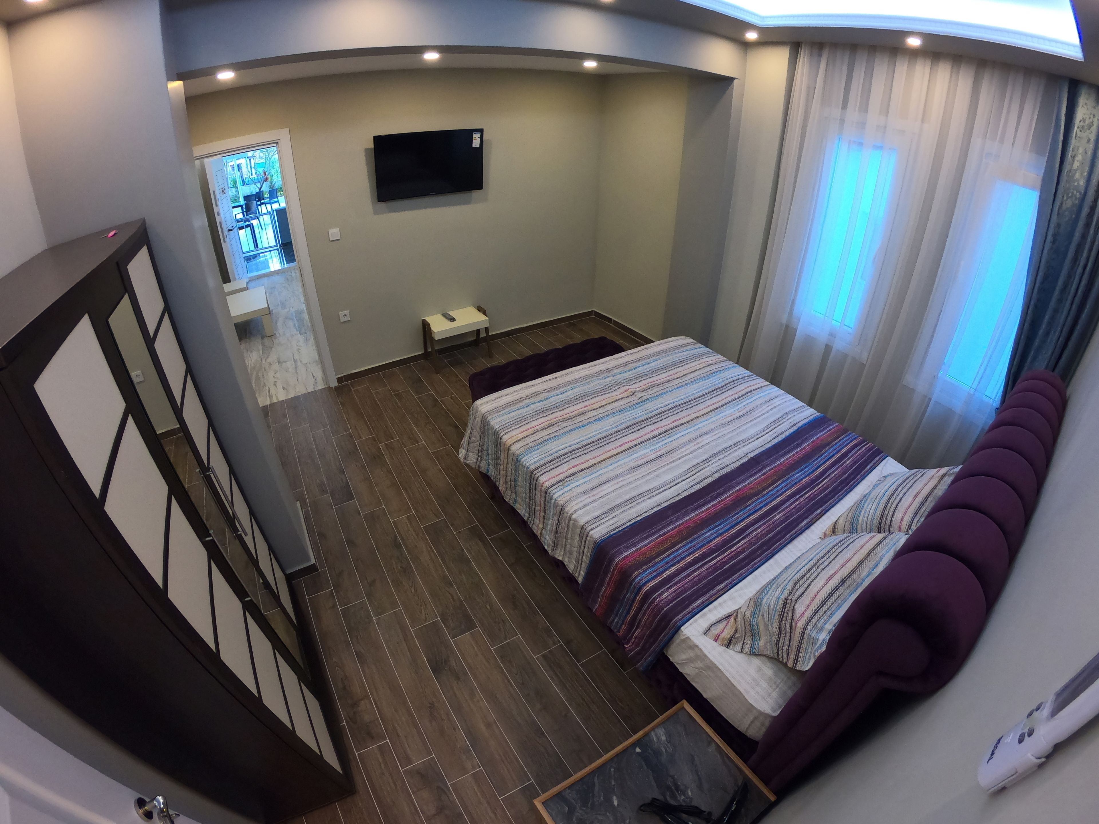A bedroom with a bed, a TV, a small table, and a window with curtains.